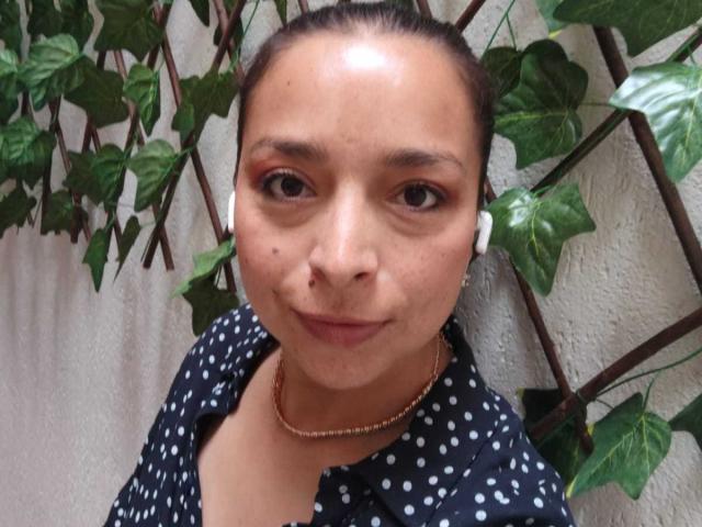 StangelarRivera has brown eyes, a small nose, and a slight smile. She wears a black polka dot shirt, a pearl necklace, and has a small mole on her right cheek.