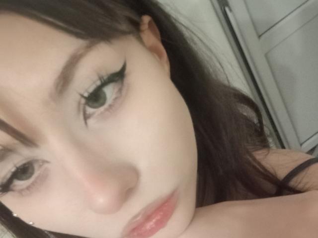 Eilene Szala hat eine blasse Haut, grünen Eyeliner und dunkelbraunes Haar. Ihre leicht geschwollenen Lippen sind leicht geöffnet, was einen subtilen, sexy Ausdruck zeigt. Ihre grünen Augen sind leicht gesenkt..