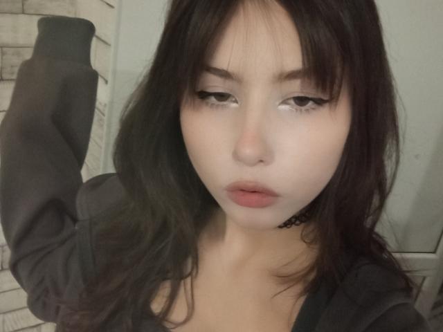 Eilene Szala, com pele clara, cabelo preto e liso, e olhos semicerrados, vestindo uma blusa preta, com uma expressão ligeiramente entediada, e um colar preto fino ao redor do pescoço..