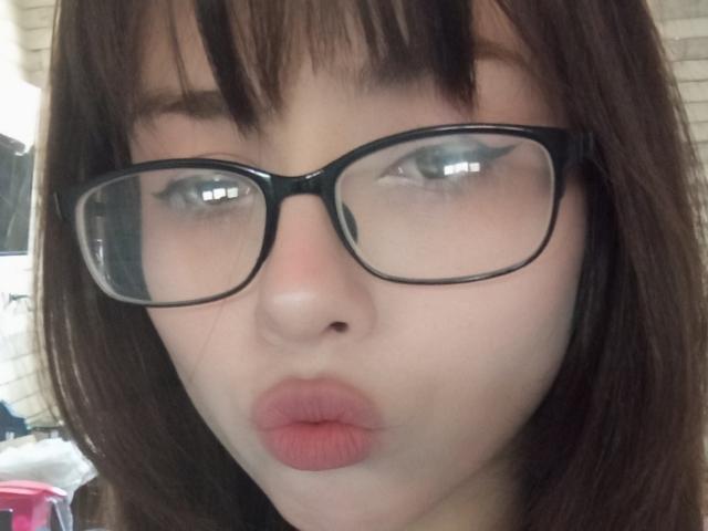 Eilene Szala hat volle, rosafarbene Lippen, trägt eine Brille mit schwarzem Rahmen, hat braunes, glattes Haar und helle Haut und blickt direkt in die Kamera. Ihre Augen sind blau..