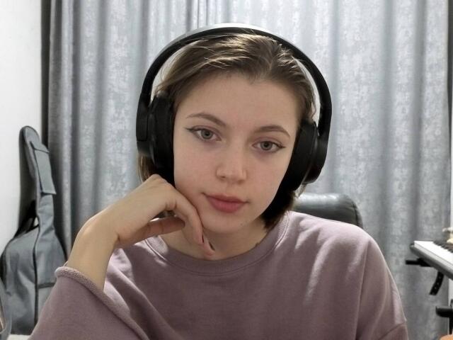 JennellMatacale with short brown hair, wearing black headphones, a purple sweater, and resting her chin on her hand, looking directly at the camera.