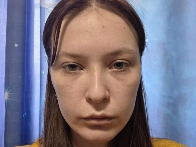 Debera Wahlers a une petite bosse sur le front, des yeux marron, des cheveux bruns lisses, une chemise jaune et une expression neutre. Son visage est légèrement brillant et on peut voir ses pores..