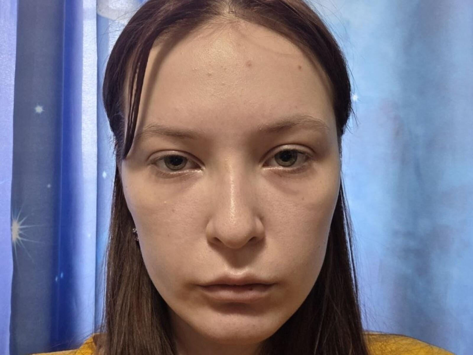 Debera Wahlers ha un brufolo sulla fronte, occhi marroni, capelli castani lisci, una camicia gialla e un'espressione neutra. Il suo viso è leggermente lucido e si vedono i pori..