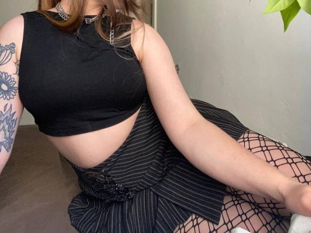 Mettis has pale skin, brown hair, and wears a black crop top, pinstriped skirt, fishnet stockings, and a choker. Her tits are medium, and she has a floral tattoo.