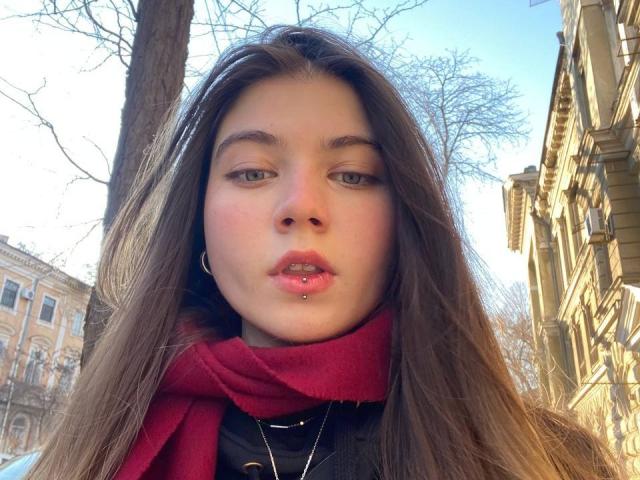 Mettis heeft lang bruin haar, een rode sjaal en een neusring, en draagt roze lippenstift. Haar groene ogen zijn iets naar beneden gericht. Ze draagt een zwarte top met een gouden ketting..