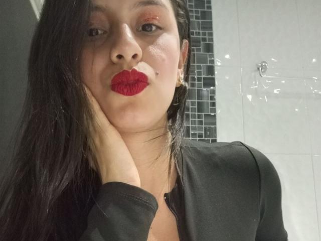 MadissonFontaine with red lipstick, black shirt, and creamy facial mask, hand on cheek, long black hair, wearing earrings, looking at camera. Her tits are not visible.