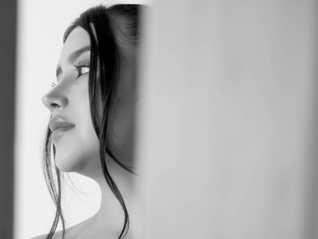 AnnaPooky's face in profile, black-and-white, with long dark hair, subtle smile, and visible eyelashes, partially obscured by a white vertical column on the right. Boobs not visible.