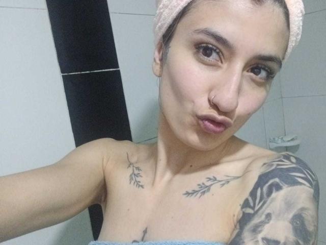 Kaiix heeft een lichte huid, tatoeages op haar schouders en een neusring. Ze maakt een zuur gezicht, draagt een handdoek op haar hoofd en laat haar kleine borsten zien..