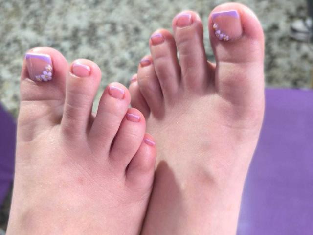 LissyCarter's feet, showing pink and purple nail polish with white dots on the big toes, in a slightly blurred photograph. Her toes are slightly dirty, with visible skin texture.