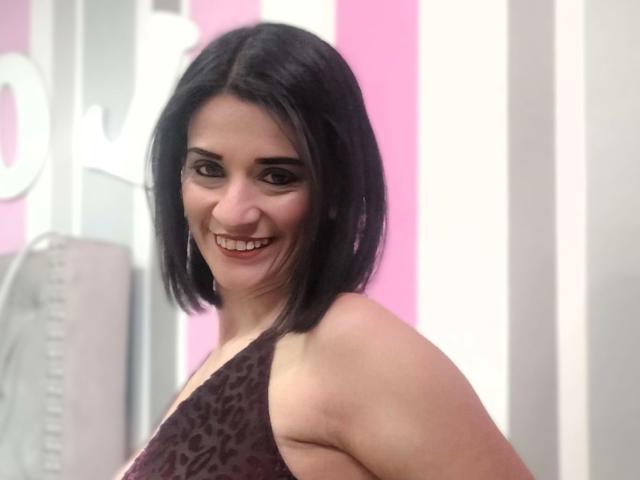 MaraRoberttss mit kurzen, schwarzen Haaren, lächelnd, zeigt ihre Brüste in einem leopardenmuster Kleid und sieht dabei süß und sexy aus. Ihr Hintern ist teilweise sichtbar. Sie ist eine süße Göre..
