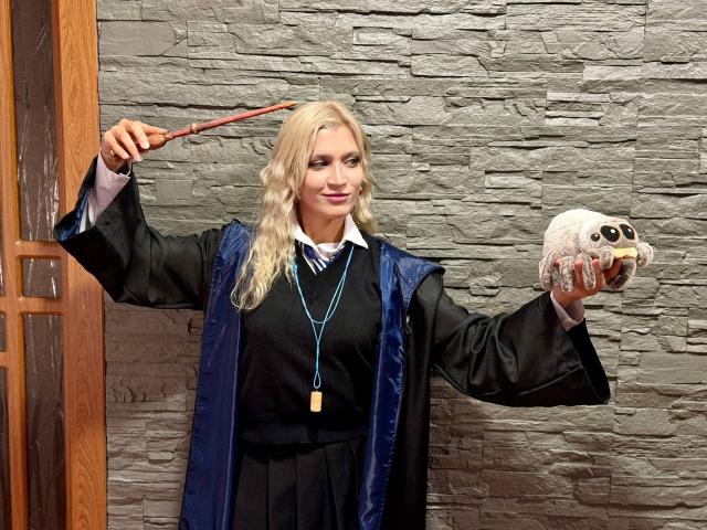RubyDavis with wavy blonde hair, wearing a black and blue wizard robe, holding a wand in one hand and a white skull with black eyes in the other.