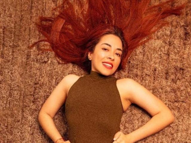 MadisonKoper with red hair, sleeveless green top, lying on brown shag carpet, smiling, hands on hips, looking up, long hair spread out, red lipstick, confident, sexy.