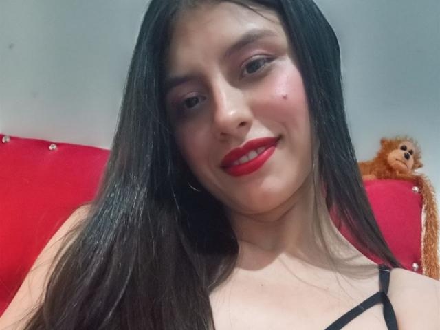 GiuliaAddams in a bathtub with rose petals, arms resting on the edge, white towel on head, red lipstick, ring on finger, blue nails, looking down, wooden walls.