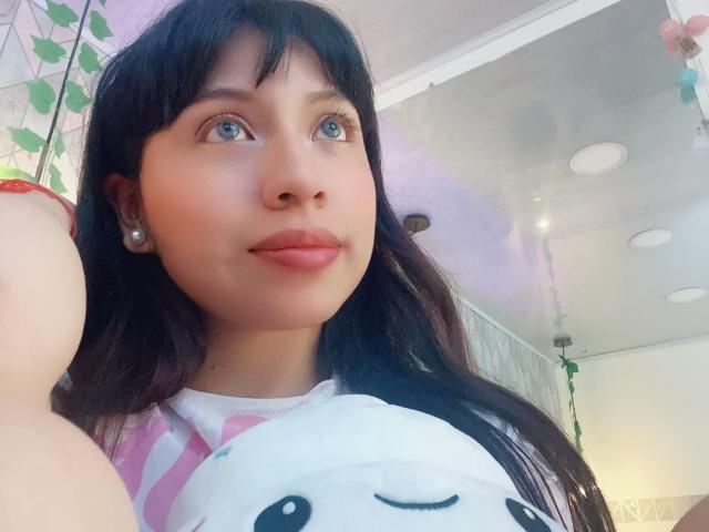 ZoeRedds with dark hair, blue eyes, and pink striped shirt, holding a white stuffed animal with a cute face, wearing pearl earrings, and a red bracelet.