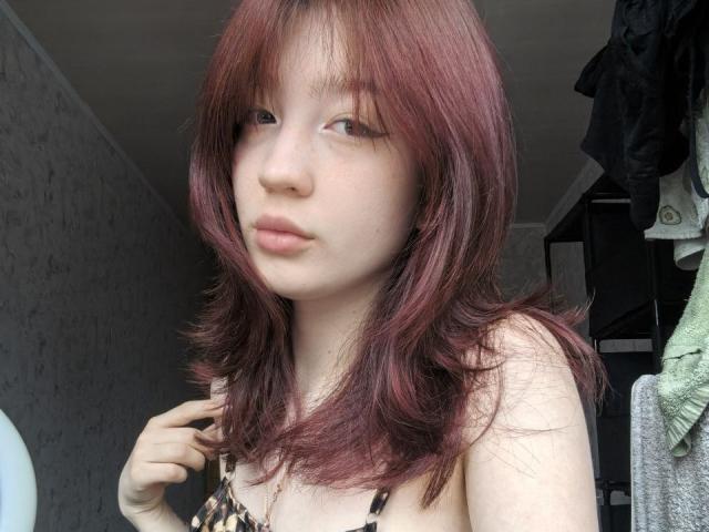 YangDariano with red-brown hair, fair skin, and small tits, wearing a leopard print top, looking slightly to the side with a neutral expression, hand near chin.