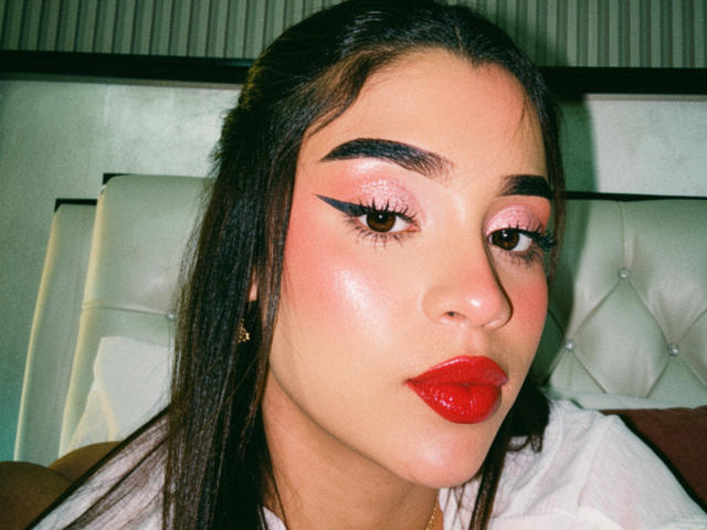 LunaVali's face with shiny pink eyeshadow, bold black eyeliner, red lipstick, and dark eyebrows. She has long black hair, a light skin tone, and a cute, pouty expression.
