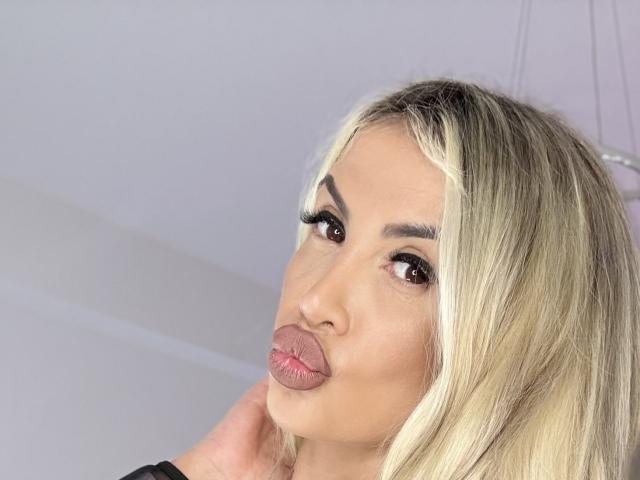 Lellie, avec ses cheveux blonds, ses lèvres roses et fines, et ses yeux marrons, a une main près de son visage, et porte du noir. Ses longs cils et son maquillage discret sont remarquables..