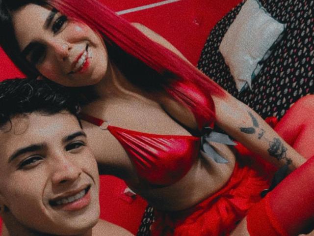 SexyCityCpl with red hair and red bikini, showing her tits, has a tattoo on her arm, smiling next to a SexyCityCpl with curly black hair, grinning.