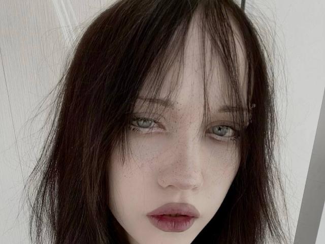 SantinaSahm has pale skin, green eyes, and dark, messy hair with bangs. She's freckled, has red lips, and a small nose. Her expression is serious and slightly sad.