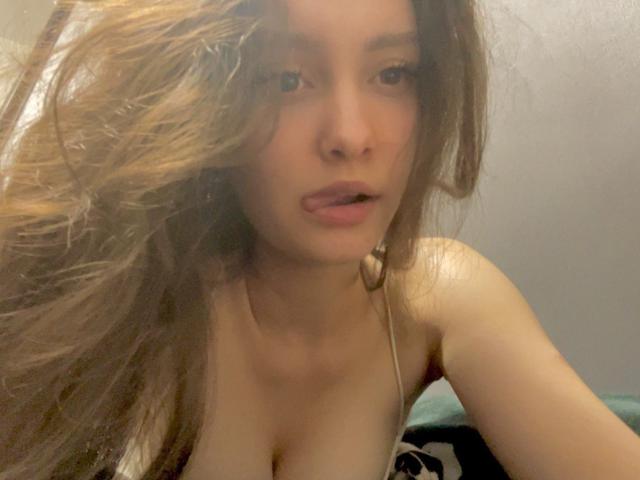 KelleyBoykin has long brown hair, light skin, and is sticking out her tongue slightly. She's wearing a strapless top, showing her small tits. The image is a selfie.
