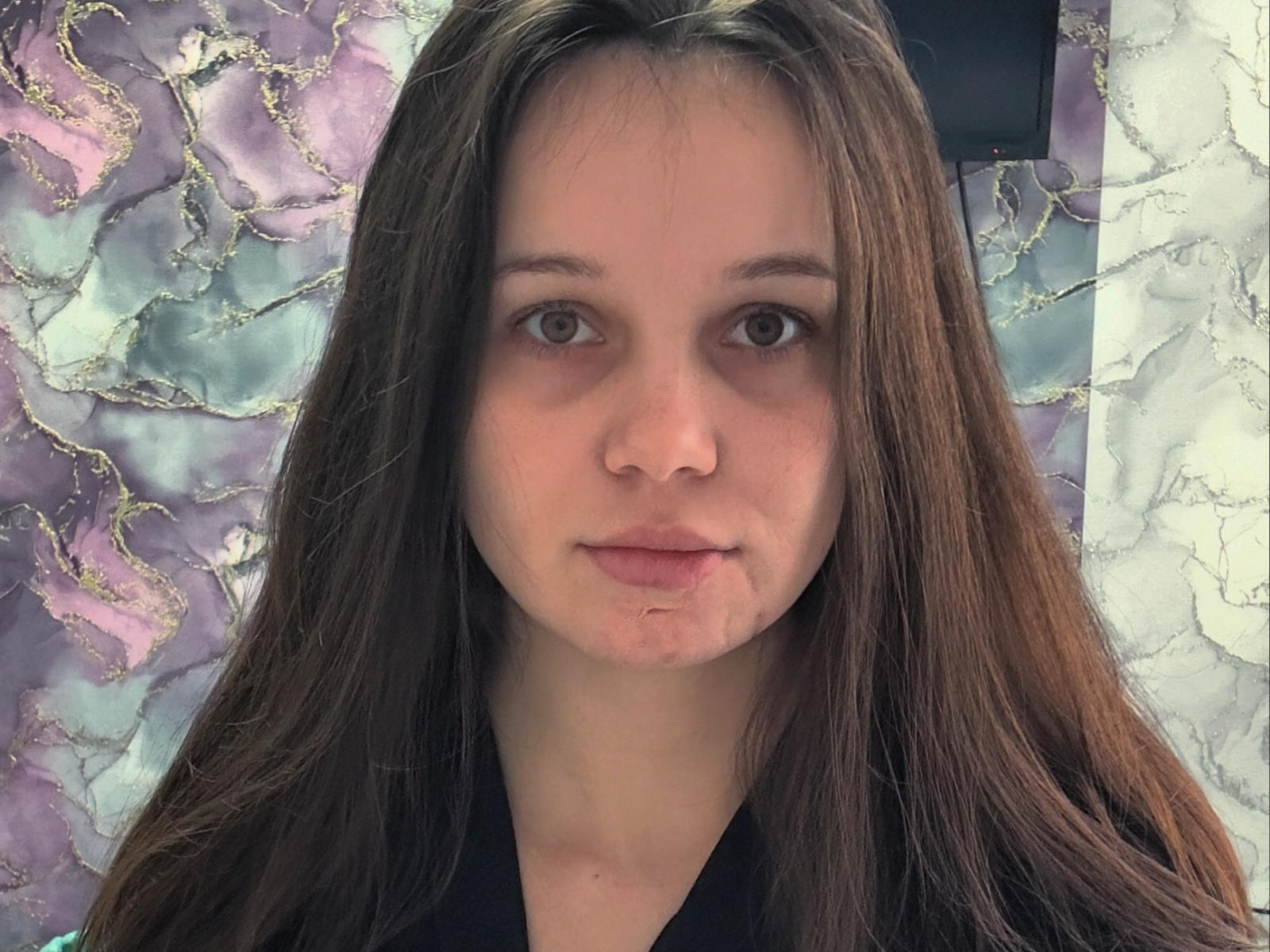 ReneBoehringer a de longs cheveux bruns, des yeux bruns et une petite coupure sur sa joue droite. Elle porte une chemise noire et regarde directement la caméra avec une expression neutre..