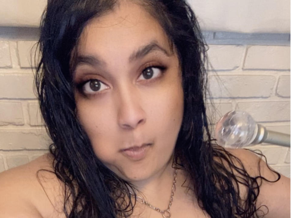 BustyBabe69 heeft nat zwart haar, bruine ogen met eyeliner, en een neutrale uitdrukking. Ze draagt een ketting, en een transparante gloeilamp is gedeeltelijk zichtbaar aan de rechterkant..