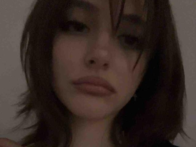 DelorisBueno's face is in the image, showing dark brown, slightly messy hair, pale skin, and full lips with a neutral expression. Her eyes are half-open, looking slightly up.