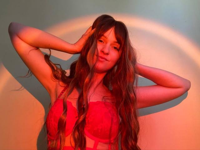 FlyFreedom with long brown hair, red lace bra, hands in hair, red-orange light, slight smile, cute, soft shadows, subtle makeup, confident, sexy.