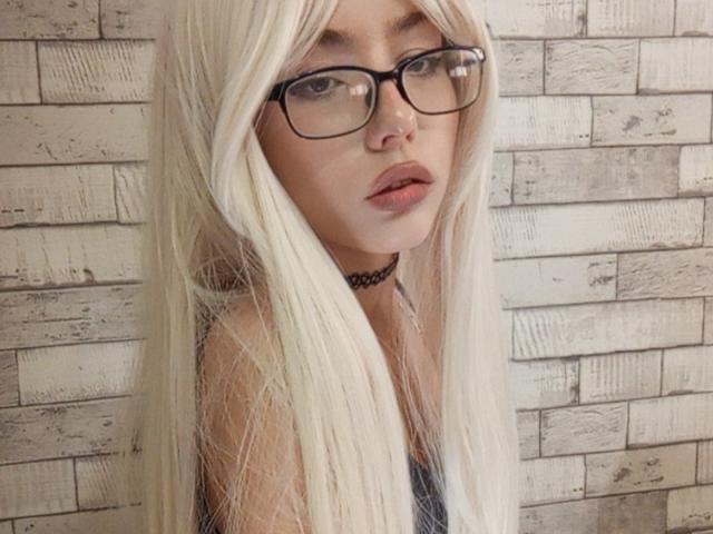 EileneSzala with long, white hair, black glasses, and a black choker, looking at the camera with slightly parted pink lips, showing a subtle nose piercing.