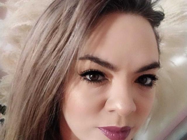 AvaMia's face, brown eyes with thick black eyelashes, pinkish-brown lipstick, and long brown hair, looking slightly to the right, with a subtle smile.
