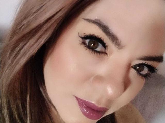 AvaMia's face, showing brown eyes with thick black eyeliner, glossy pinkish-purple lipstick, and smooth fair skin. She has brown hair and a slight smile.