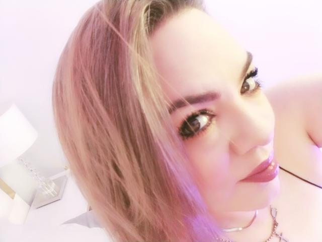 AvaMia with pinkish-brown hair, large brown eyes, and pink lipstick, sticking out her tongue. She's wearing a choker and has a sexy, playful expression.