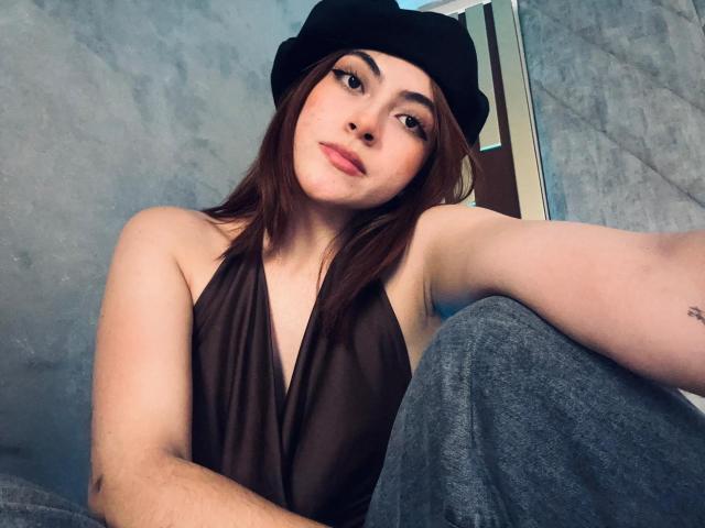 SpencerLe, con i capelli castani, il cappello nero e la maglietta nera trasparente, che mostra il seno in un selfie, seduta con i jeans blu, le labbra leggermente tumefatte e un tatuaggio discreto sul braccio..
