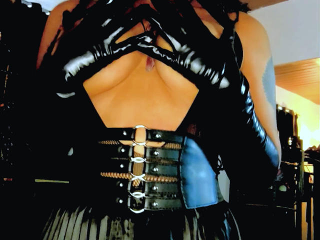 DivaMarie with shiny black latex gloves, chest exposed, showing tits, wearing a black leather corset with metal buckles and straps, in a dark, sexy, BDSM-inspired outfit.