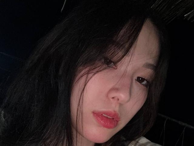 CatherinaKicker has pale skin, black hair, and pink lips. Her eyes are slightly downcast, and her hair is messy, partially covering her face. She's looking relaxed.