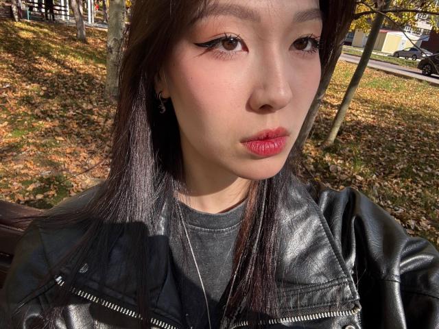 CatherinaKicker has pale skin, dark straight hair, black eyeliner, pink lipstick, black leather jacket, and a serious expression. Her small tits are partially visible under the jacket.