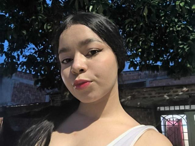 LissyCarter has light brown skin, black hair in a ponytail, white sleeveless top, and pink lipstick. She's looking at the camera with a slight pout.