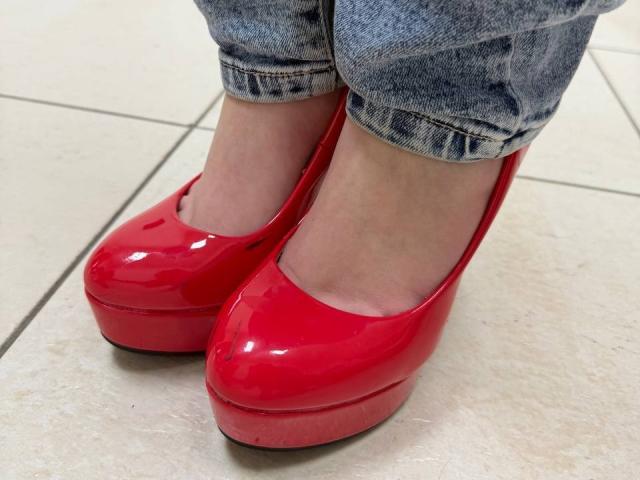 VikkiRi's shiny red high heels with thick platforms, standing on beige tiles, wearing slightly frayed blue jeans with cuffs rolled up. Her ankles are visible.