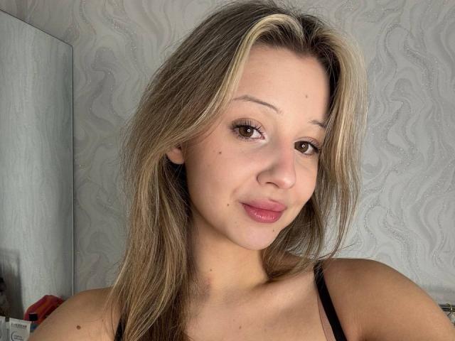 MerrieHamad heeft blond haar met donkere aanzet, bruine ogen, roze lippen en kleine borsten. Ze draagt een zwarte top en heeft een lichte glimlach. Haar huid is licht..