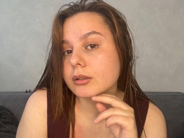 EvelinaNewsom has wet brown hair, light skin, and brown eyes, with slightly parted lips and a hand near her chin, wearing a sleeveless maroon top.