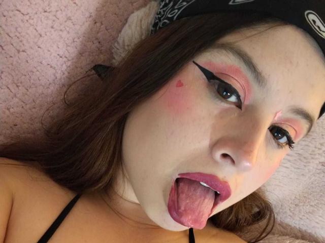 Melani Becker ha il trucco rosa, l'eyeliner nero e un piccolo tatuaggio a forma di cuore sulla guancia. Ha la lingua fuori e indossa una bandana nera in testa..