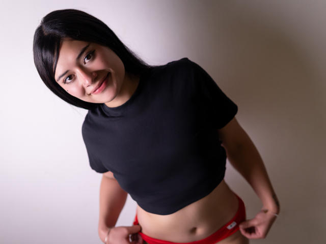 AmbarLandry with black crop top, smiling, dark hair, medium skin, small tits, red panties, hands on hips, standing, looking up, soft lighting, casual, confident, cute.