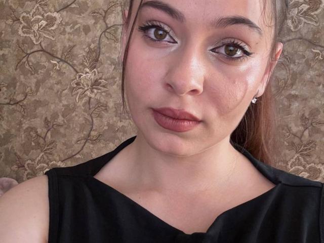 SyreetaTippetts with pouty lips, brown eyes, and long eyelashes, wearing a black top, has a fair skin tone, brown hair in a ponytail, and small stud earrings.