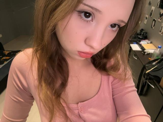 MarceneMalatesta, con le labbra piene, gli occhi marroni e i lunghi capelli castani, indossa una maglietta a coste rosa che mette in mostra il suo seno piccolo, in un selfie scattato con un leggero angolo di ripresa rivolto verso l'alto..