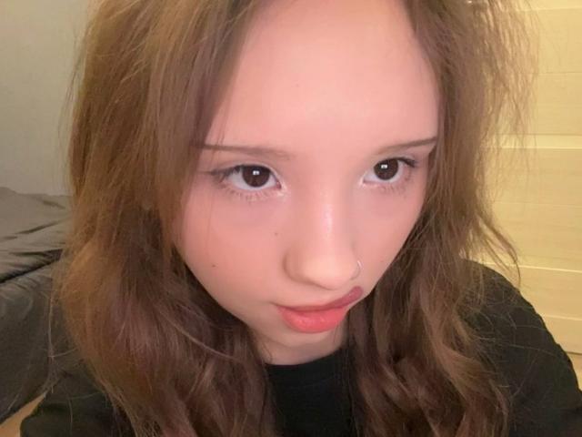 MarceneMalatesta tem cabelos castanho-claros e ondulados, um pequeno piercing no nariz e lábios rosados e carnudos. Seus olhos castanhos estão voltados para frente com uma expressão ligeiramente curiosa. Ela está vestindo uma blusa preta..