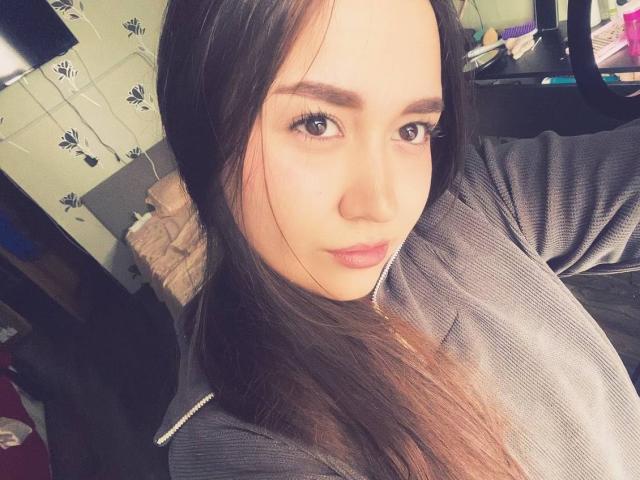Classie Cotham, con cabello largo y castaño oscuro, vestida con una camisa gris con cremallera, tiene una cara linda, una nariz pequeña y labios rosados y gruesos, con una ligera sonrisa, mirando a la cámara..