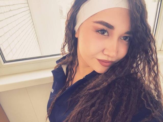 ClassieCotham with curly brown hair, wearing a white headband and navy shirt, has blue eyes, full eyebrows, and a slight smile, showing a cute, relaxed face.