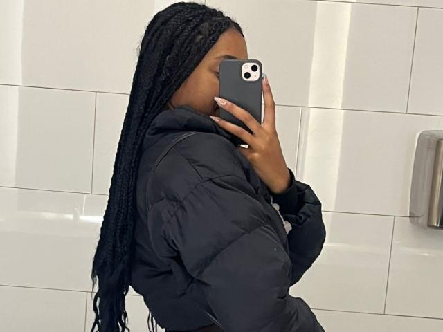 EsmeraldaRoe with long black braids, wearing a black puffy jacket, taking a mirror selfie with a grey iPhone, showing a side profile, with her ass slightly visible.