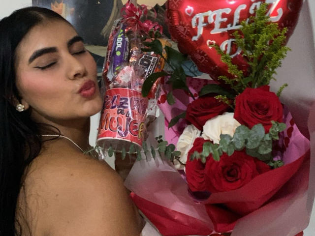 AlaraKey with pouty lips, dark eyebrows, and long black hair, next to a red heart and bouquet of red and white roses, and a beer can.