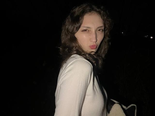 LeonieRahim with curly brown hair, pouty lips, and a white long-sleeve shirt, holding a bag, in a dark night setting, looking over her shoulder.